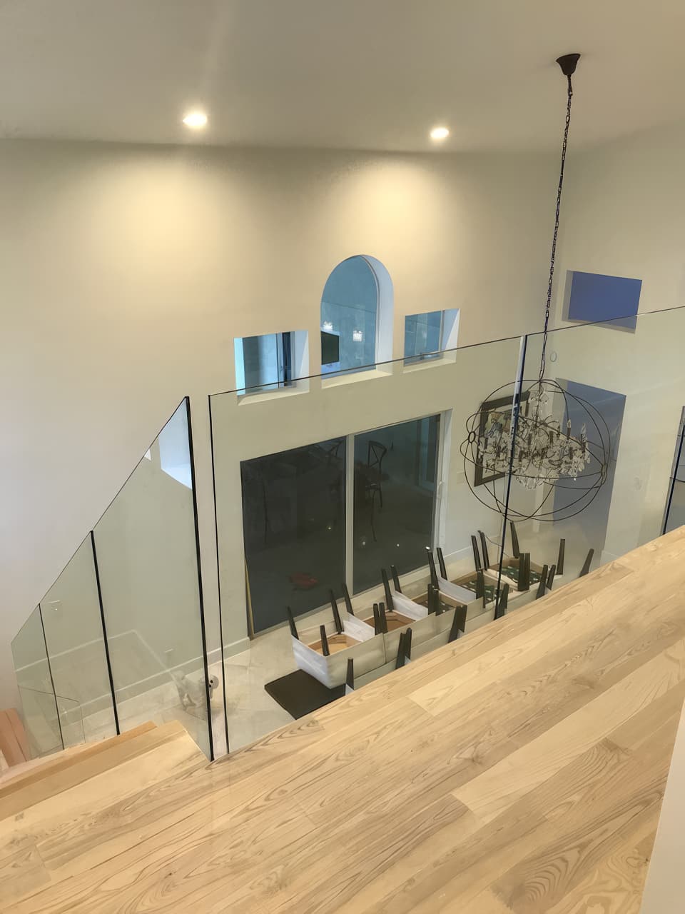 View from the landing through the frameless glass rail, down to the dining table and the orb chandelier.